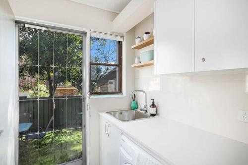 a white kitchen with a sink and a window at Ocean Cove - cosy retreat steps from beach & cafes in Mollymook