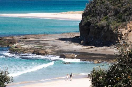 two people walking on a beach near the ocean at Aloha Kioloa in Kioloa