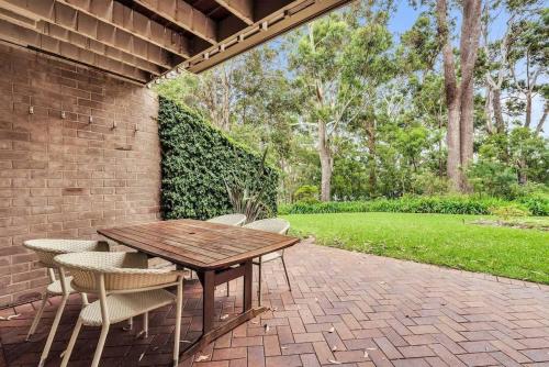 a wooden table and chairs on a brick patio at Riversdale Retreat - w. beach & golf course access in Mollymook