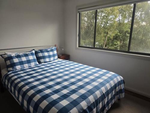 a bedroom with a blue and white bed with a window at Bawley Backyard Haven - family retreat near beach in Bawley Point