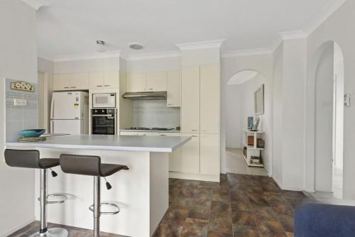 una cocina blanca con encimera y 2 taburetes en Reflections, en Conjola