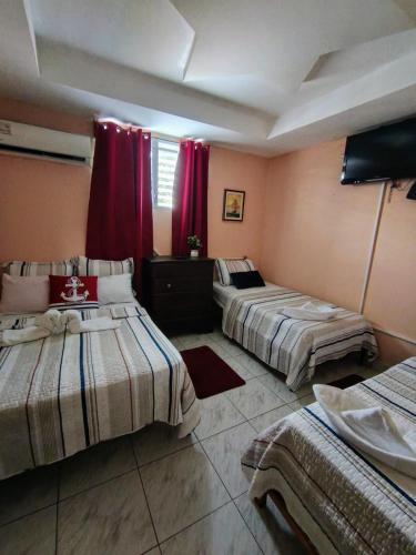 three beds in a room with red curtains at Hotel Pensión Galicia in Obaldía