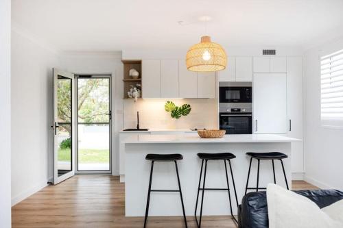 a kitchen with white cabinets and bar stools at Sandy Shores in Mollymook