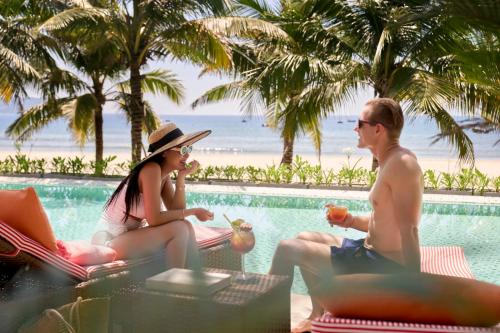 a group of people sitting next to a swimming pool at Signature by M Village Beachfront Hotel in Da Nang