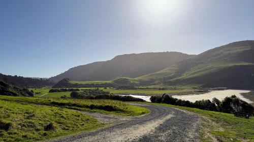 a dirt road in a valley with a river and mountains at Mohua Park - Catlins Eco Accommodation in Owaka