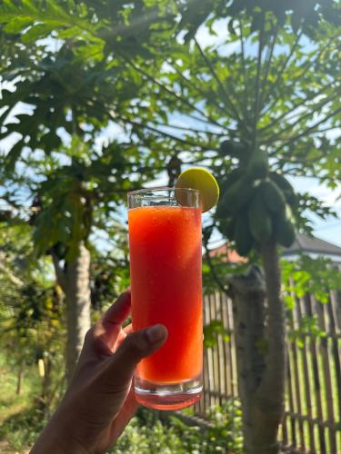 a person holding a glass with a orange drink at Sriwedari House Keramas in Gianyar