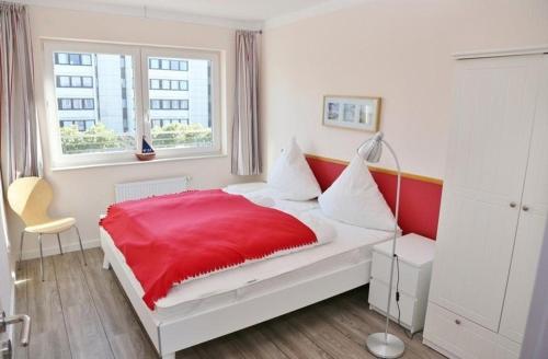 a white bedroom with a red bed with a window at Am Rundsteg 8 in Burgtiefe auf Fehmarn 