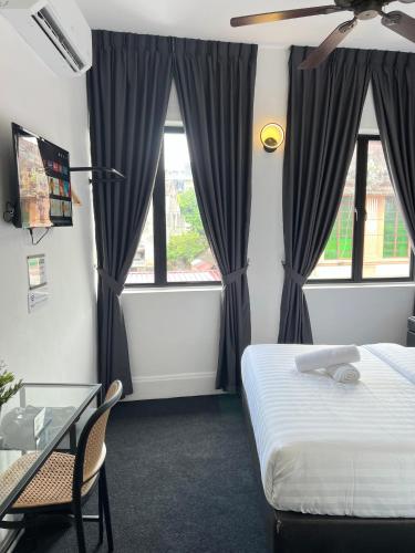 a bedroom with a bed and a table and windows at Quee Hotel in George Town