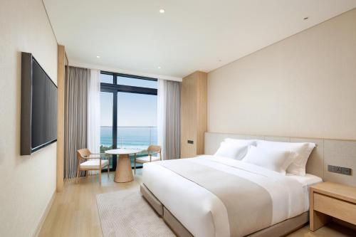 a bedroom with a large white bed and a table at Shillamonogram Gangneung Hotel in Gangneung