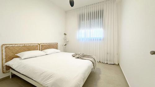 ein Schlafzimmer mit einem Bett mit weißen Laken und einem Fenster in der Unterkunft דירת פאר מול חוף הים in H̱adera
