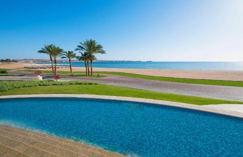 a swimming pool next to a beach with palm trees at Baron Palace Sahl Hasheesh in Hurghada