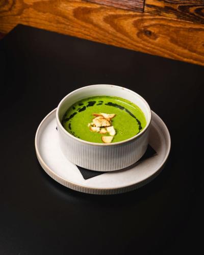 a bowl of green soup on a white plate at Aparthotel Koroni Home in Raszyn