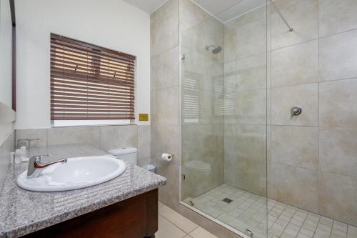 a white bathroom with a shower and a sink at Umthunzi Hotel and Conference in Umtentweni