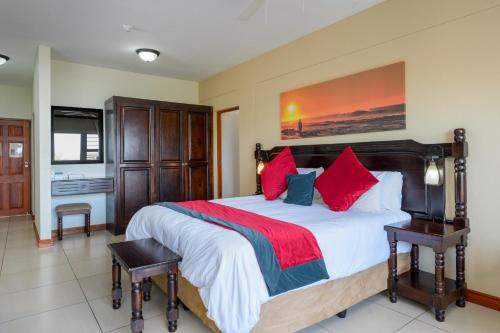 a bedroom with a large bed with red pillows at Umthunzi Hotel and Conference in Umtentweni