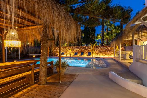 a swimming pool with a straw umbrella and benches at Villa Clara Ibiza in Santa Eularia des Riu