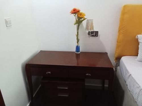 a vase with a flower on a table next to a bed at Lake 47 Suites Ltd in Abuja