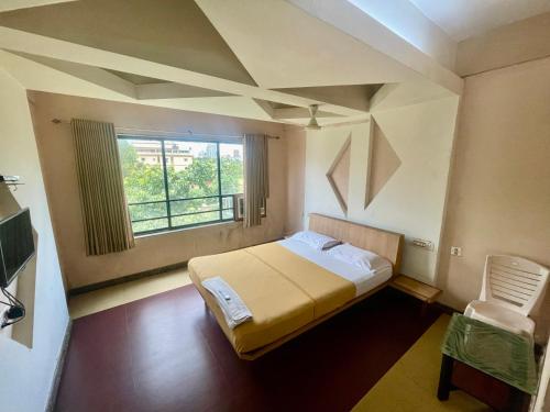ein Schlafzimmer mit einem Bett, einem Fenster und einem Stuhl in der Unterkunft Hotel Shambhavi in Udupi