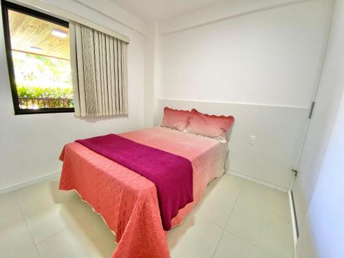 a white bedroom with a bed with a pink blanket at Lindo Flat Garden beira-lago e perto da praia in Camaçari