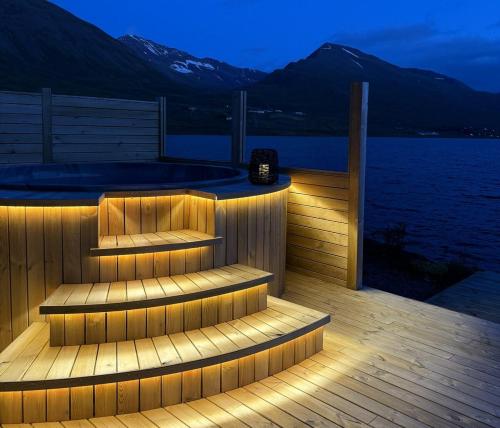 a deck with a hot tub and stairs next to the water at Bakkabyggd - A lake view villa in Ólafsfjörður