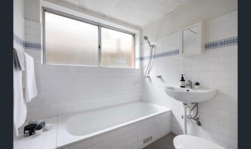 a white bathroom with a tub and a sink at Ground Level Apartment with Pool in Sydney