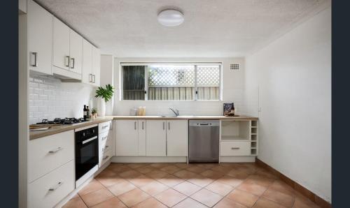 a kitchen with white cabinets and a window at Ground Level Apartment with Pool in Sydney