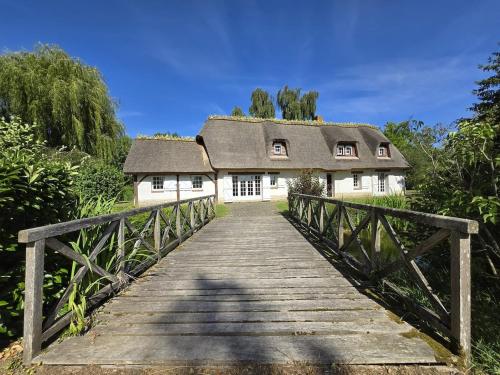 a bridge leading to a house with a roof at Chaumière entre rivière & champs, piscine privée in Verneuil d’Avre et d’Iton