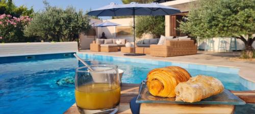 a glass of orange juice and bread on a table next to a pool at Le Masdemoiselle Mazet in Salernes