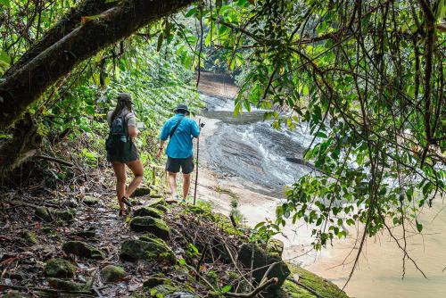 two people walking down a trail next to a river at El Jardin Lodge & Spa in Puerto Misahuallí