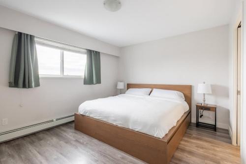 a white bedroom with a large bed and a window at Soothing Minimalist Escape - Suite with Balcony & Fireplace in Vancouver