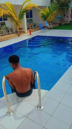 a man sitting in a chair next to a swimming pool at Bleu Marin Résidence hôtelière in Hila-Kondji