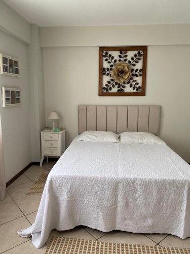 a bedroom with a white bed and a clock on the wall at Apartamento com piscina a poucos passos da praia in Niterói