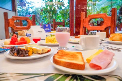 a table with plates of food and a glass of milk at VELINN Feiticeira Praia Hotel in Ilhabela