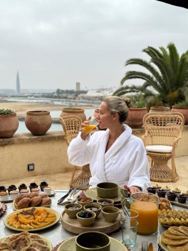 a woman drinking a glass of orange juice at a table of food at Riad Dar Baraka Rabat in Rabat