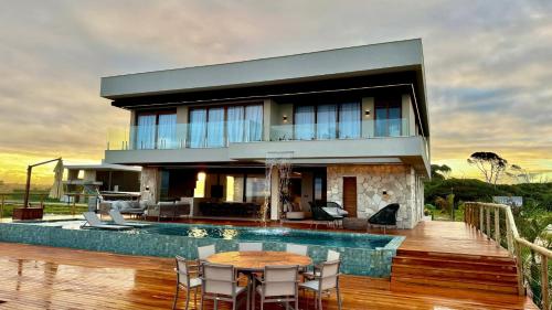 ein Haus mit einem Pool, einem Tisch und Stühlen in der Unterkunft Mansão Pé na Areia 8 Suítes Alphaville Guarajuba in Barra de Jacuípe