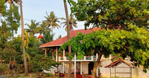 a house with a red roof and palm trees at Marari Praise Beachfront Homestay in Mararikulam