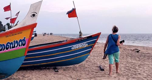 a woman standing next to a boat on a beach at Marari Praise Beachfront Homestay in Mararikulam