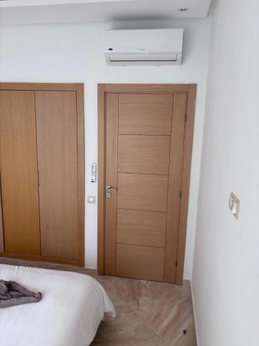 a bedroom with two wooden doors and a bed at Shems Bouznika Residence Central & Cozy 2 Bedroom Apartment with Pool Bouznika in Bouznika