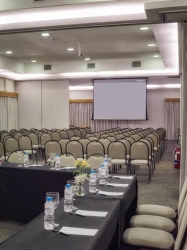 a conference room with tables and chairs and a white screen at FLAT 1805 - SOL Alphaville Hotel e Residence Barueri in Barueri