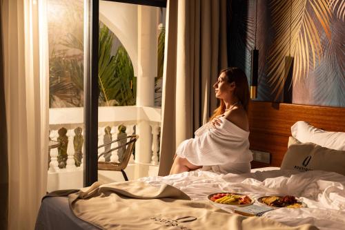 a woman sitting on a bed with a plate of food at Q Boutique Resort Malindi in Malindi