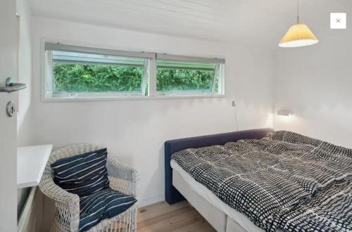 a bedroom with a bed and a chair and two windows at Lovely Summerhouse By Skaastrup Strand W Sea View in Bogense