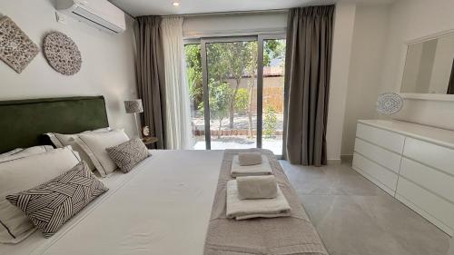 a bedroom with a large white bed with a large window at Kantara Garden Apt by TrulyCyprus in Limassol