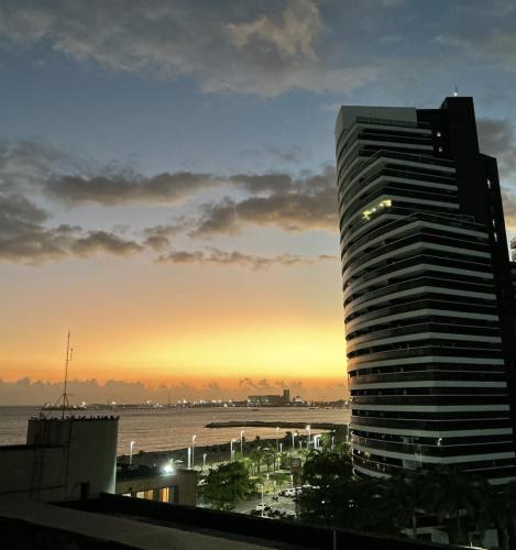 Flat Beira Mar - Fortaleza في فورتاليزا: مبنى شاهق بجوار المحيط عند غروب الشمس