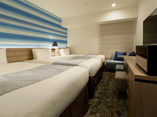 a hotel room with four beds and a television at Mitsui Garden Hotel Hiroshima in Hiroshima