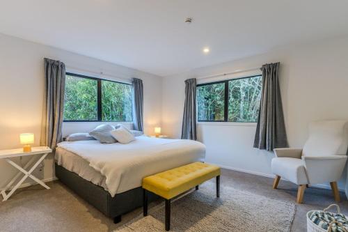 Un dormitorio con una cama y una silla y ventanas. en Harbour Retreat at St Leonard's, en Dunedin
