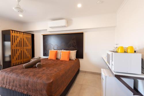 1 dormitorio con 1 cama con almohadas de color naranja y TV en Safari Lodge Motel, en Tennant Creek