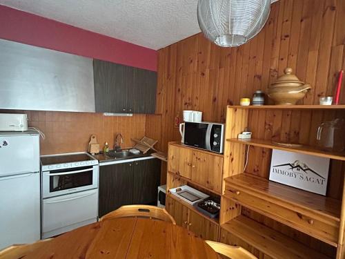 Il comprend une cuisine dotée de murs en bois, d'une table et d'un réfrigérateur. dans l'établissement Appartement 2 pièces au cœur de la station - FR-1-814-65, à Besse-et-Saint-Anastaise