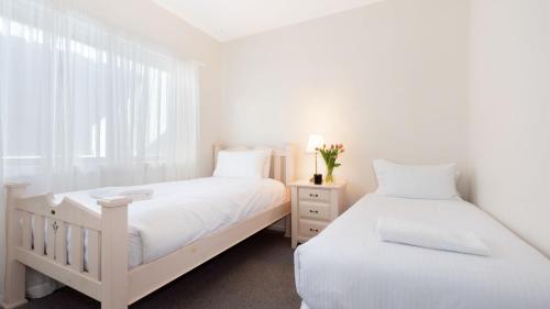 two beds in a white bedroom with a window at Summit to Sea in Kiama