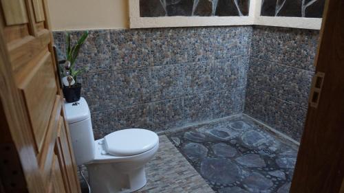 a bathroom with a toilet and a stone wall at Biorock Homestay & Dive Center Pemuteran in Pemuteran