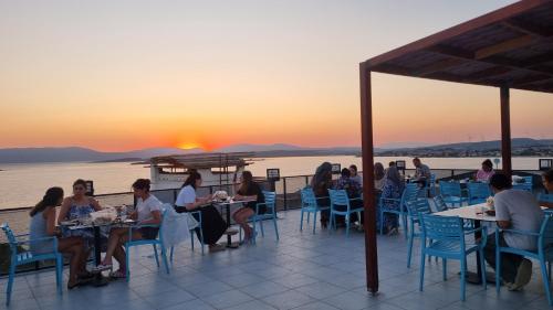 a group of people sitting at tables on a deck with a sunset at Ugem in Seferihisar