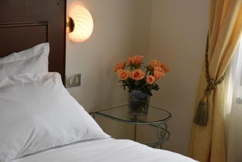 a vase of orange roses on a glass table next to a bed at Hotel Livio in Brescia